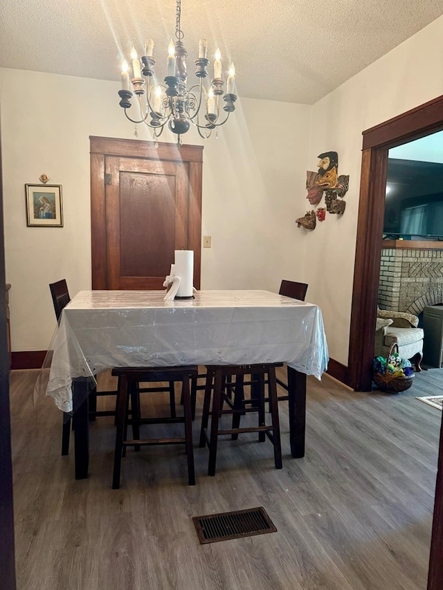 dining area with baseboards, wood finished floors, a textured ceiling, and a notable chandelier