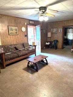 living area featuring tile patterned floors, a ceiling fan, and wooden walls