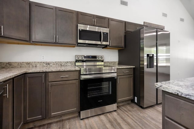 kitchen featuring appliances with stainless steel finishes, light wood-style flooring, dark brown cabinets, and light stone counters