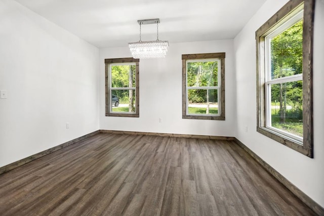 unfurnished dining area featuring plenty of natural light, dark wood-type flooring, a chandelier, and baseboards