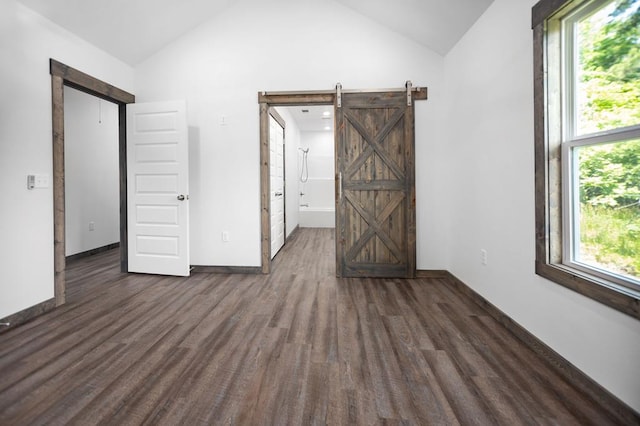 unfurnished bedroom with a barn door, lofted ceiling, wood finished floors, multiple windows, and baseboards