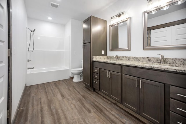 bathroom with wood finished floors, toilet, double vanity, and  shower combination