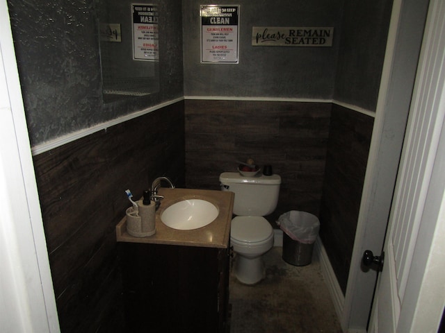 bathroom with vanity, wood walls, and toilet