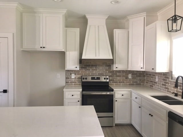 kitchen featuring white cabinetry, sink, stainless steel appliances, premium range hood, and decorative light fixtures