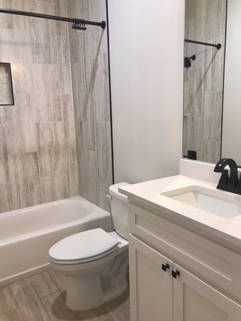 full bathroom featuring hardwood / wood-style flooring, vanity, toilet, and tiled shower / bath combo