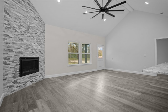 unfurnished living room featuring hardwood / wood-style floors, a stone fireplace, ceiling fan, high vaulted ceiling, and beam ceiling