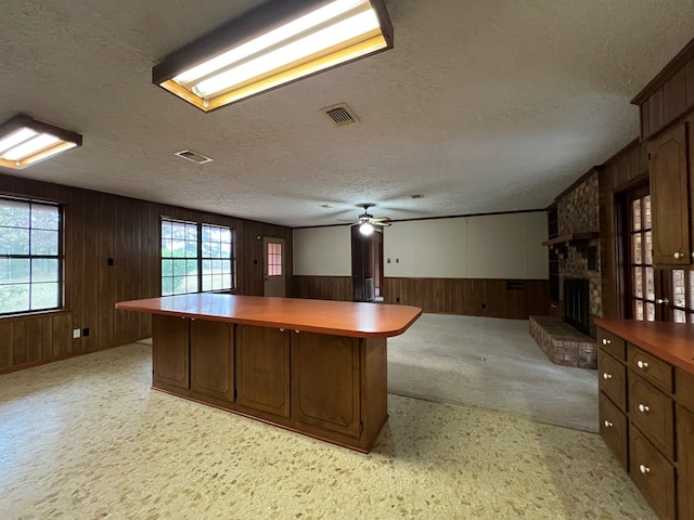 unfurnished office featuring a textured ceiling, light colored carpet, ceiling fan, wooden walls, and a fireplace