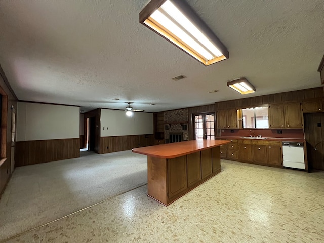 kitchen featuring a fireplace, a textured ceiling, wooden walls, dishwasher, and a kitchen island