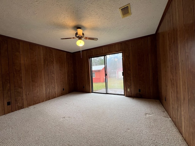 carpeted empty room with a textured ceiling, ceiling fan, and wooden walls