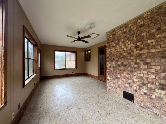 empty room featuring ceiling fan, wood walls, and a textured ceiling