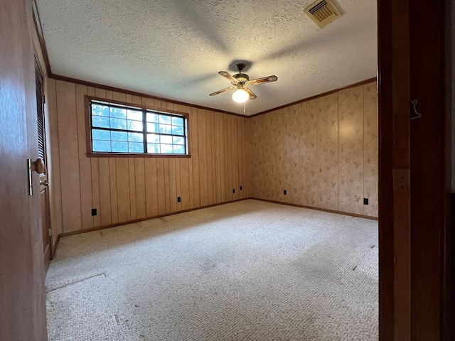 carpeted empty room featuring ceiling fan, wooden walls, and a textured ceiling