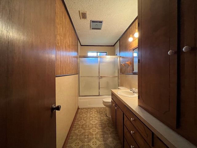 full bathroom with toilet, shower / bath combination with glass door, a textured ceiling, and wooden walls