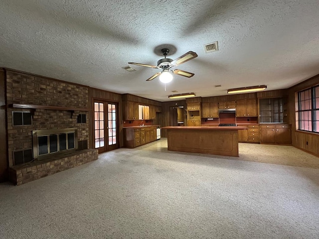 kitchen with french doors, a brick fireplace, wood walls, light colored carpet, and a textured ceiling