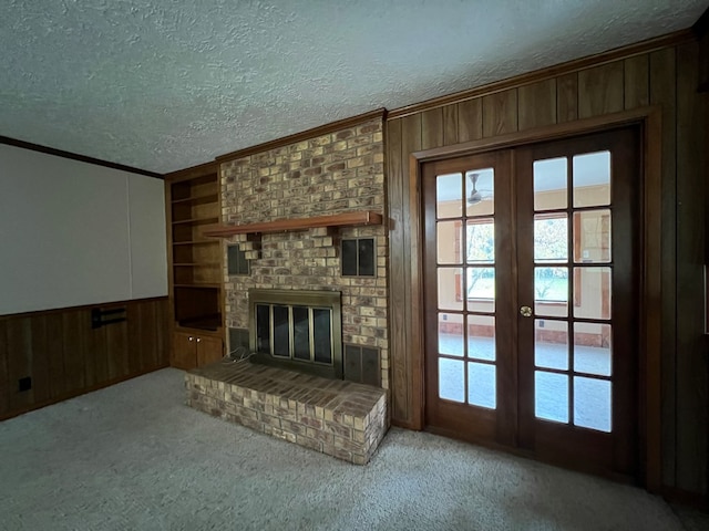 unfurnished living room with french doors, light carpet, a brick fireplace, a textured ceiling, and wooden walls