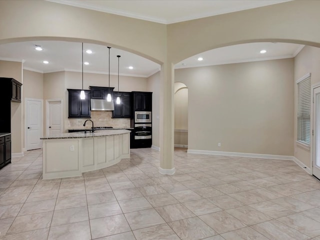 kitchen featuring stainless steel microwave, hanging light fixtures, light stone counters, a center island with sink, and exhaust hood