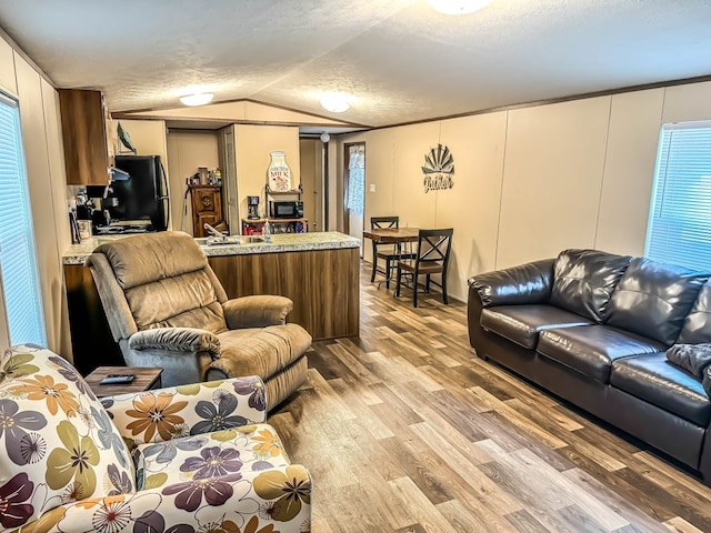 living room featuring a textured ceiling, sink, light hardwood / wood-style flooring, and vaulted ceiling