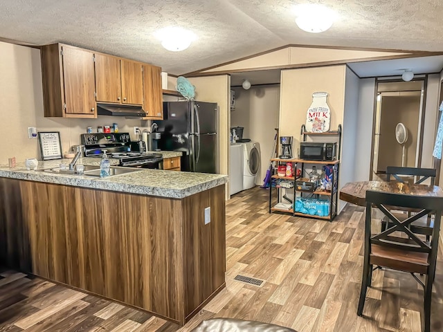 kitchen with black appliances, washer and dryer, vaulted ceiling, and light hardwood / wood-style floors