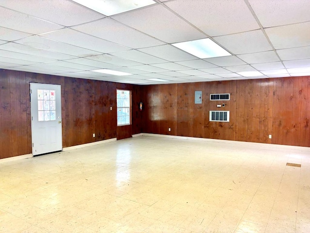 spare room featuring a drop ceiling, plenty of natural light, and wood walls