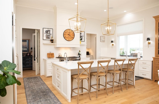 kitchen featuring white cabinetry, a center island with sink, light hardwood / wood-style floors, and decorative light fixtures