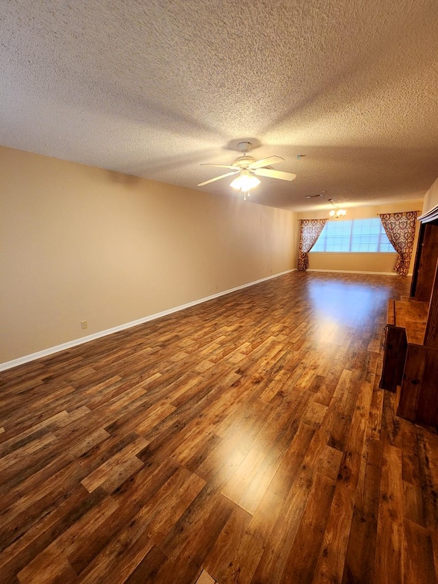 unfurnished living room featuring dark wood-type flooring, a textured ceiling, baseboards, and a ceiling fan