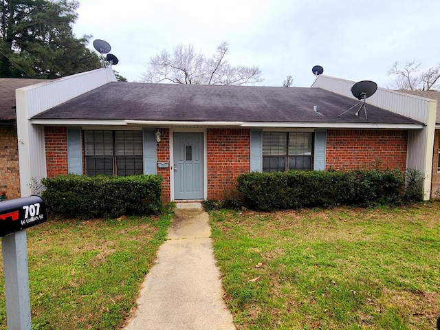 ranch-style house featuring a shingled roof, a front yard, and brick siding