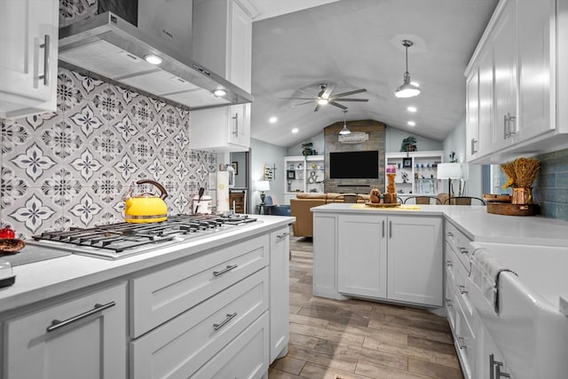 kitchen featuring stainless steel gas stovetop, white cabinetry, wall chimney range hood, and decorative light fixtures