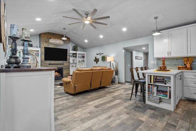 living room with ceiling fan, light wood-type flooring, lofted ceiling, and a fireplace