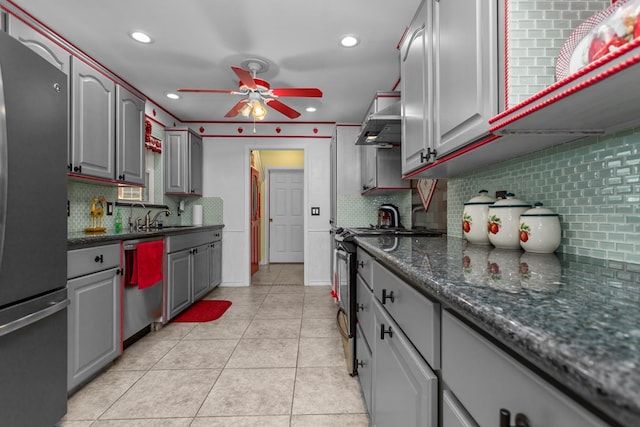 kitchen with tasteful backsplash, gray cabinetry, stainless steel appliances, ceiling fan, and wall chimney range hood