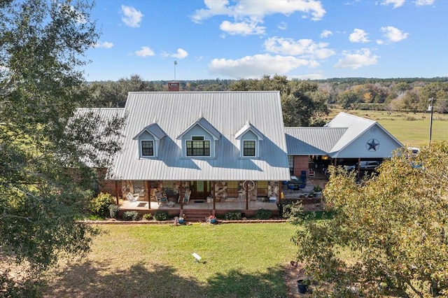 view of front facade with a chimney, a front lawn, covered porch, a carport, and metal roof