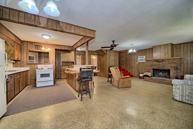 kitchen with white appliances, hanging light fixtures, wooden walls, a brick fireplace, and ceiling fan