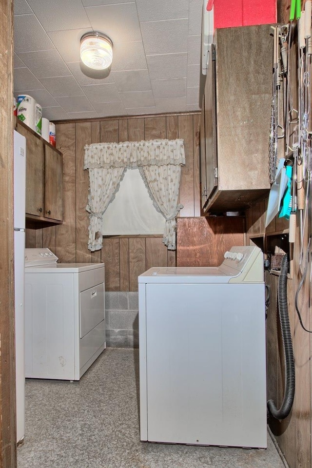 laundry area featuring washing machine and dryer, wooden walls, and cabinets