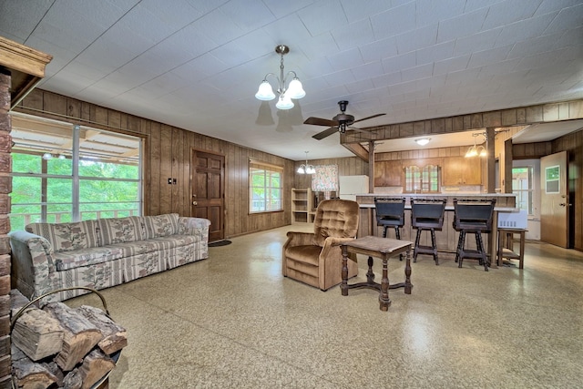 living room featuring ceiling fan with notable chandelier and wooden walls