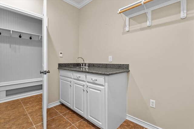 laundry area with dark tile patterned floors, crown molding, and sink