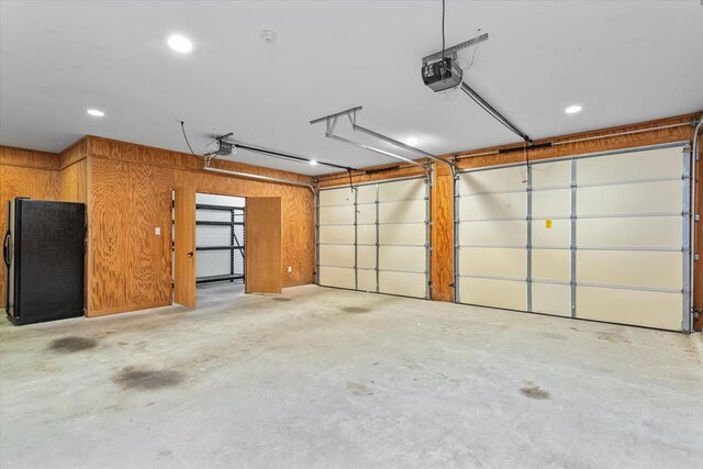 garage featuring black refrigerator, a garage door opener, and wooden walls