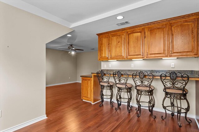 kitchen featuring ceiling fan, a kitchen breakfast bar, kitchen peninsula, and dark wood-type flooring