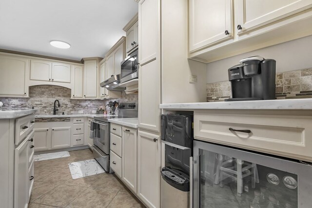 kitchen with backsplash, stainless steel appliances, sink, light tile patterned floors, and cream cabinetry