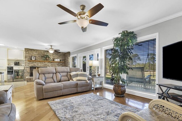 living room featuring ceiling fan, light hardwood / wood-style floors, a stone fireplace, and ornamental molding