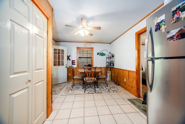 dining space featuring ceiling fan, light tile patterned flooring, ornamental molding, and wooden walls