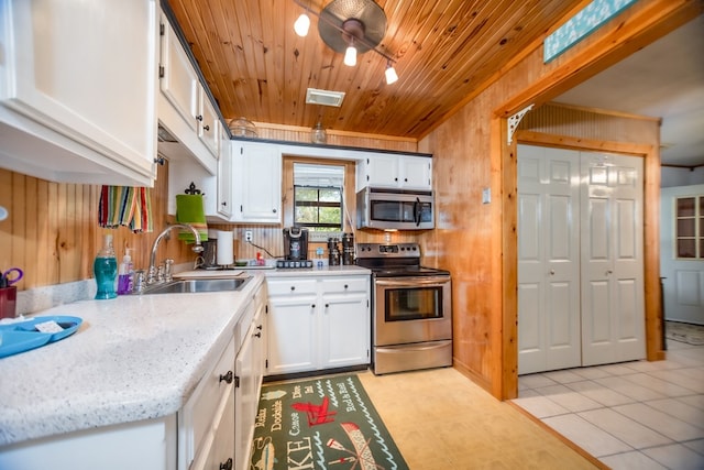 kitchen with appliances with stainless steel finishes, wood ceiling, sink, white cabinets, and wood walls