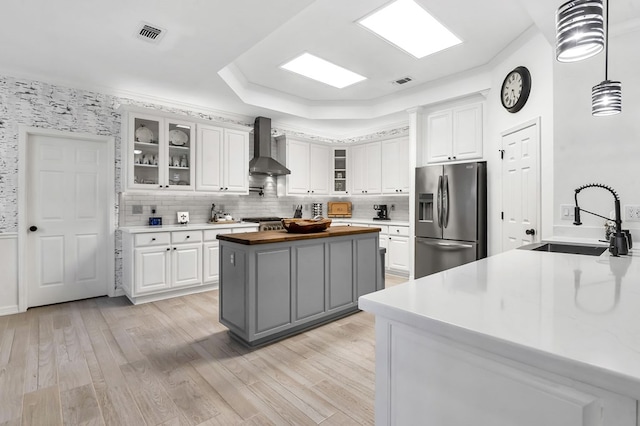 kitchen with wall chimney exhaust hood, sink, white cabinetry, and stainless steel appliances