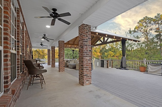 patio terrace at dusk featuring an outdoor living space, ceiling fan, and a deck