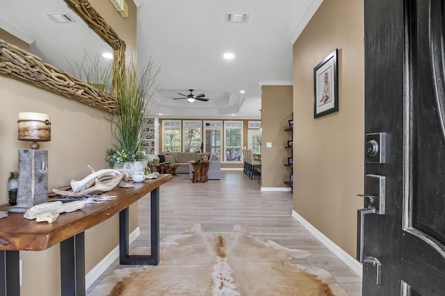 hall featuring light hardwood / wood-style floors, crown molding, and a tray ceiling