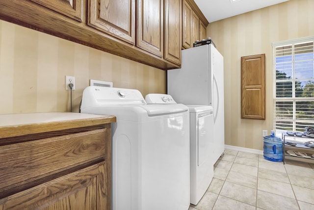 clothes washing area with cabinets, light tile patterned floors, and washing machine and clothes dryer