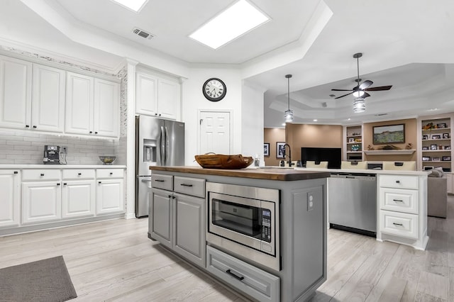 kitchen featuring light wood-type flooring, a tray ceiling, a kitchen island, white cabinetry, and stainless steel appliances