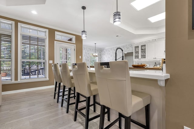 kitchen with a kitchen breakfast bar, light hardwood / wood-style floors, white cabinetry, and hanging light fixtures