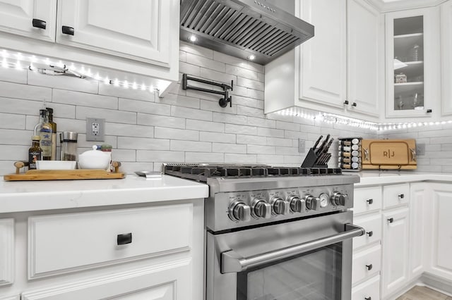 kitchen with tasteful backsplash, high end stainless steel range, white cabinets, and wall chimney range hood