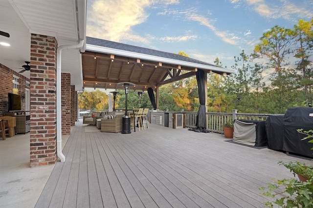 deck at dusk featuring an outdoor hangout area, area for grilling, ceiling fan, an outdoor bar, and a grill