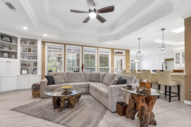 living room with light wood-type flooring, a tray ceiling, and ornamental molding