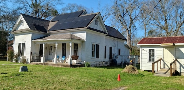 exterior space featuring covered porch, an outdoor structure, solar panels, and a front yard