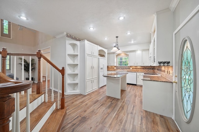 kitchen with a center island, pendant lighting, a textured ceiling, white appliances, and light hardwood / wood-style floors